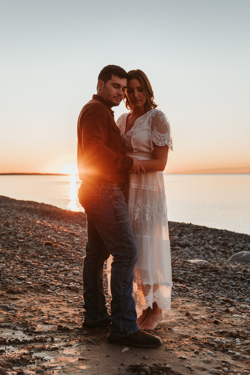 couple embrace on lakeshore at sunset