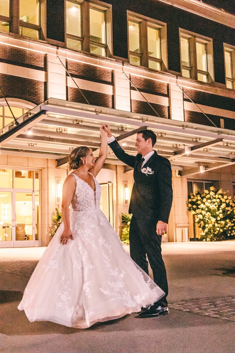 A newlywed couple joyfully dancing outside a hotel at night in Davenport, with the bride in a white gown and the groom in a tuxedo.