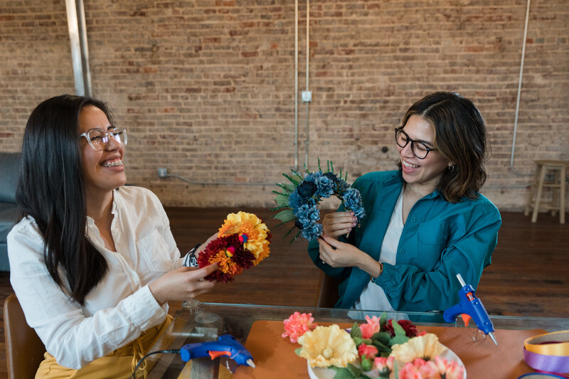 Women create art in our artistic workshop, surrounded by colorful flowers in shades of orange and blue. Seated on a glass desk adorned with captivating art objects, their happiness is contagious.
