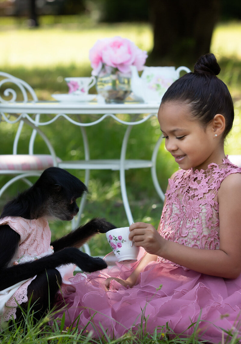 girl-in-pink-couture-dress-sitting-with-monkey-in-front-of-tea-party-set-in arlington-tx