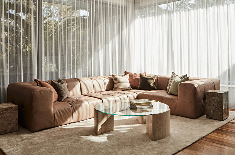 Contemporary living room with tan sectional sofa, glass coffee table, and sheer curtains – residential interior design Melbourne