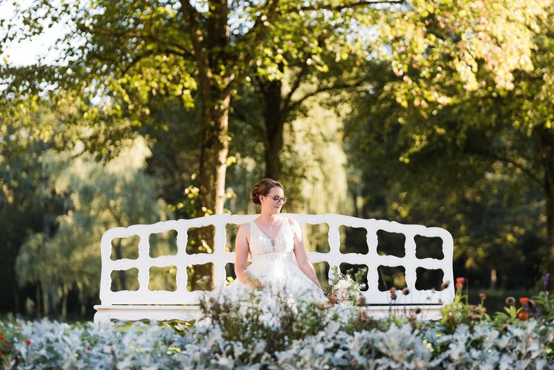 Braut sitz auf Bank und hält ihr Blumenstrauss Schloss Lustheim Schloss Schleißheim Hochzeitsfotograf  Starnberg