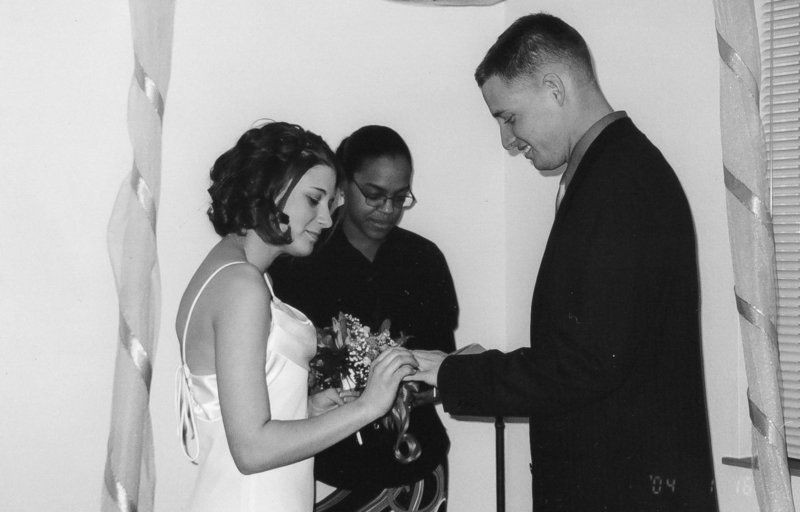 A couple exchanges rings during a destination wedding ceremony while an officiant observes.