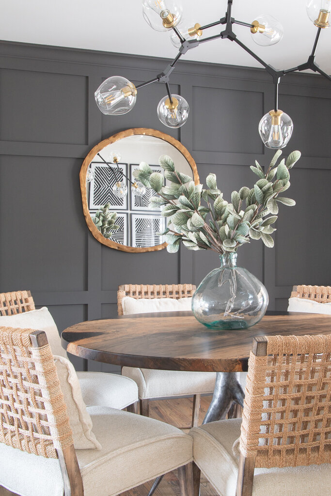Detail shot of a dining room featuring a charcoal accent wall, round mirror, round dining table, and woven back chairs designed by Chapin SC interior designer Haven + Harbor