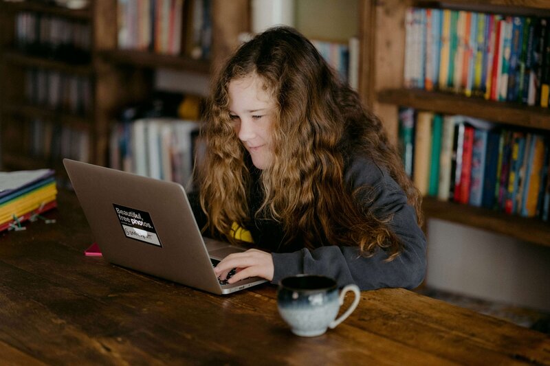 A student completing online tutoring at her desk with books in the background
