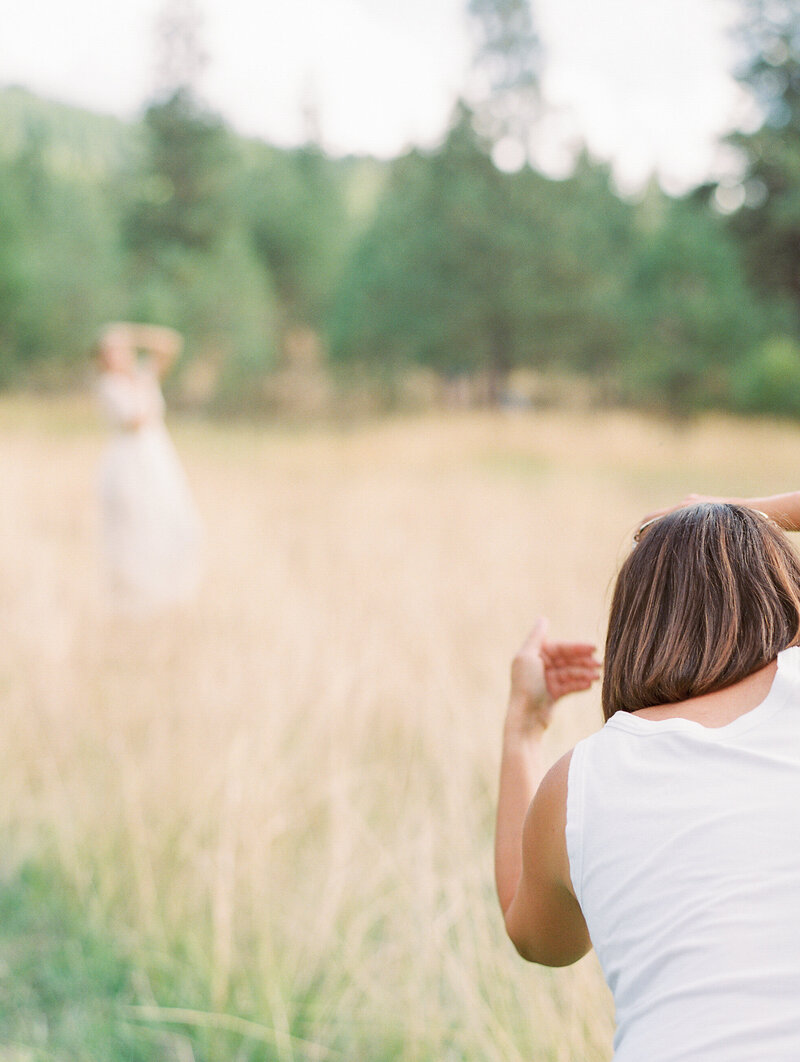 Wedding photographer guides bride posing in outdoor field