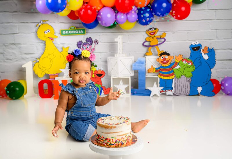 little girl in overalls smashes her birthday cake in her studio cake smash