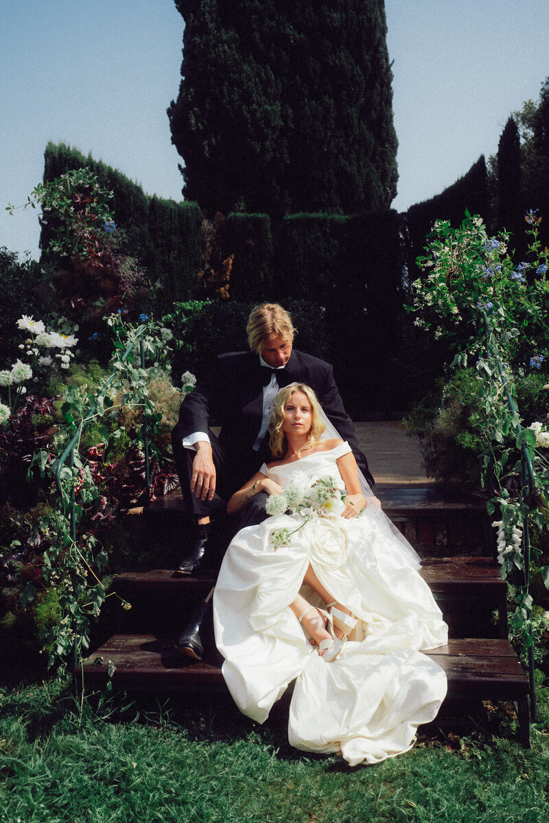 Bride and groom sitting together in a sunlit Italian garden, captured in a romantic, cinematic style by a luxury destination wedding photographer UK.