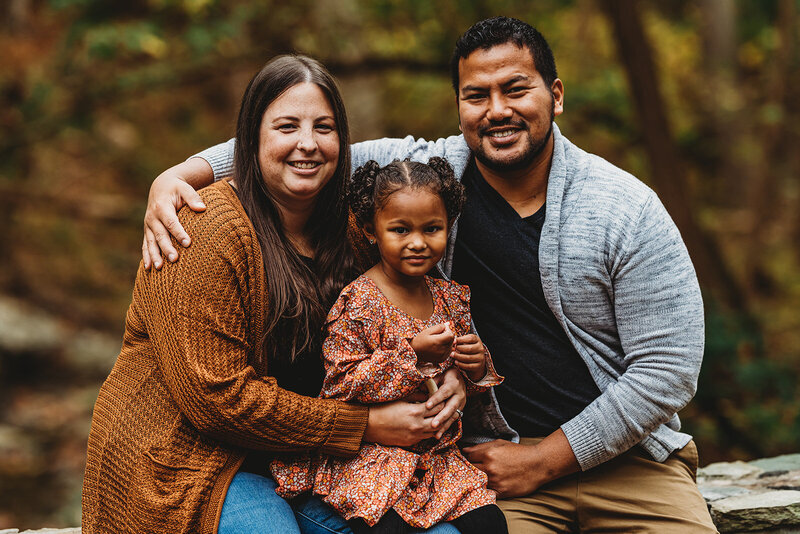 Family photographers Maryland captures fall family photos with parents sitting together with their small child sitting on the mother lap