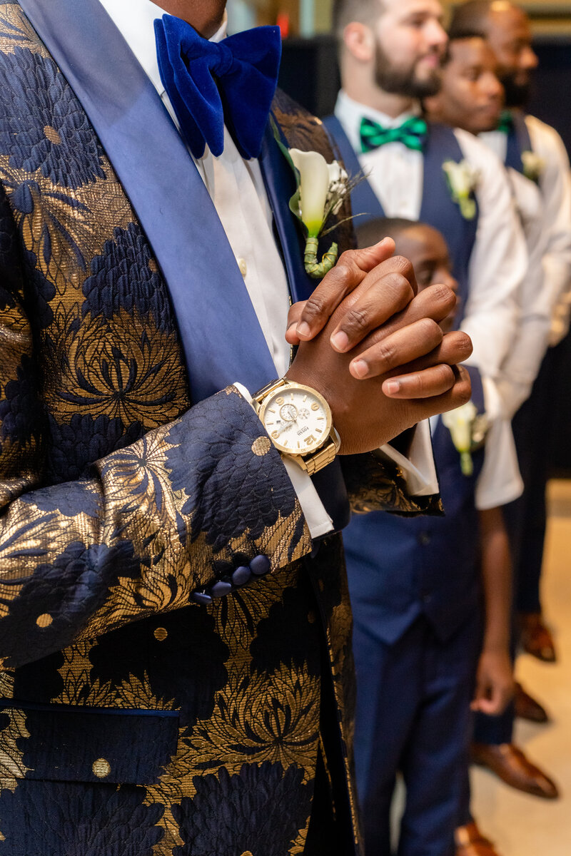 A wedding party of black groomsmen. the groom hands are folded with a gold watch in focus. Wedding colors are blue and goldA wedding party of black groomsmen. His hands are folded with a gold watch in focus. The wedding colors are blue and gold.