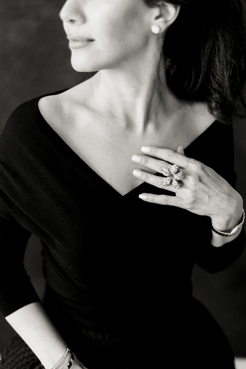 Close up black and white boudoir photo of a woman wearing a black dress and she delicately touches her chest while posing in a Dallas photography studio.