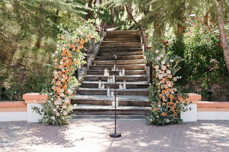 Wedding ceremony floral arch pillars with blush and peach flowers  in front of a wooden staircase at Rancho Las Lomas in Orange County California