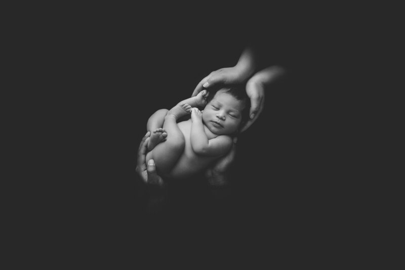 newborn baby sleeping black and white photo with parents hands holding head and bottom