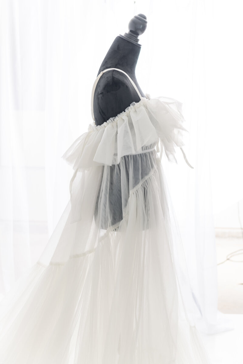 A white sheer maternity gown hangs on a mannequin