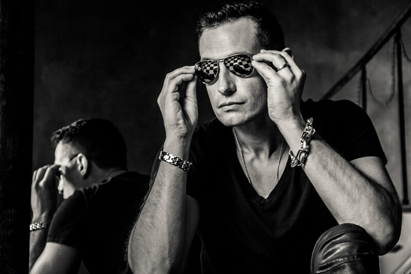 Black and White Musician Portrait Adam Rutledge Nashville sitting while holding sunglasses  he wears that have reflection of black and white tiles