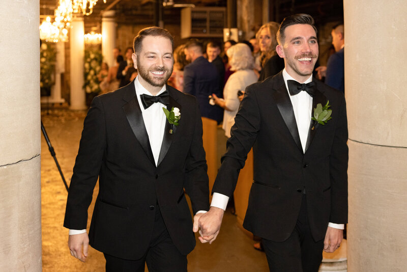 Two men smile while holding hands exiting their wedding ceremony.