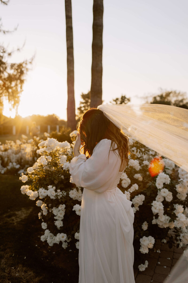 Catholic bride walks among flower bushes during golden hour