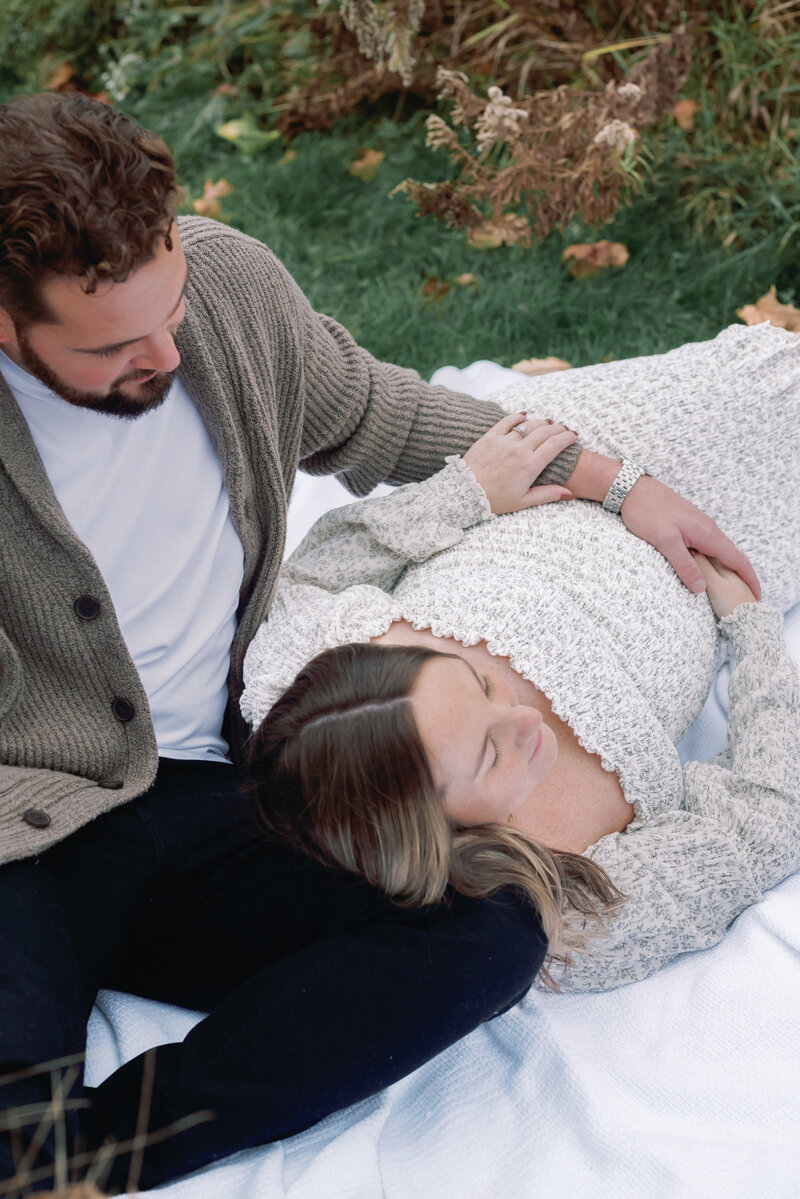 Expecting mom laying down outside on partner's lap for maternity session