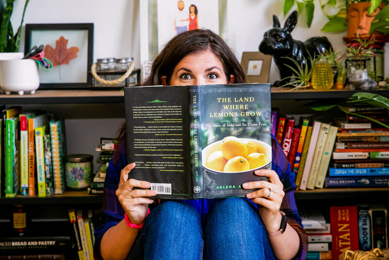 Woman looks over the top of her book, The land Where Lemons Grow
