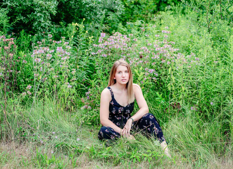 high school senior girl in black floral romper sitting in wildflower field at ionia state recreational park in ionia michigan