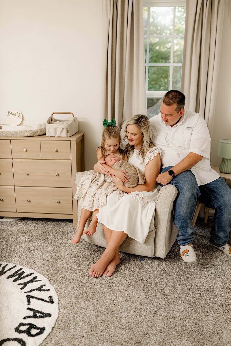 Mother snuggles her newborn son with her daughter sitting beside her and her husband behind her in their Charlotte home during their lifestyle newborn session