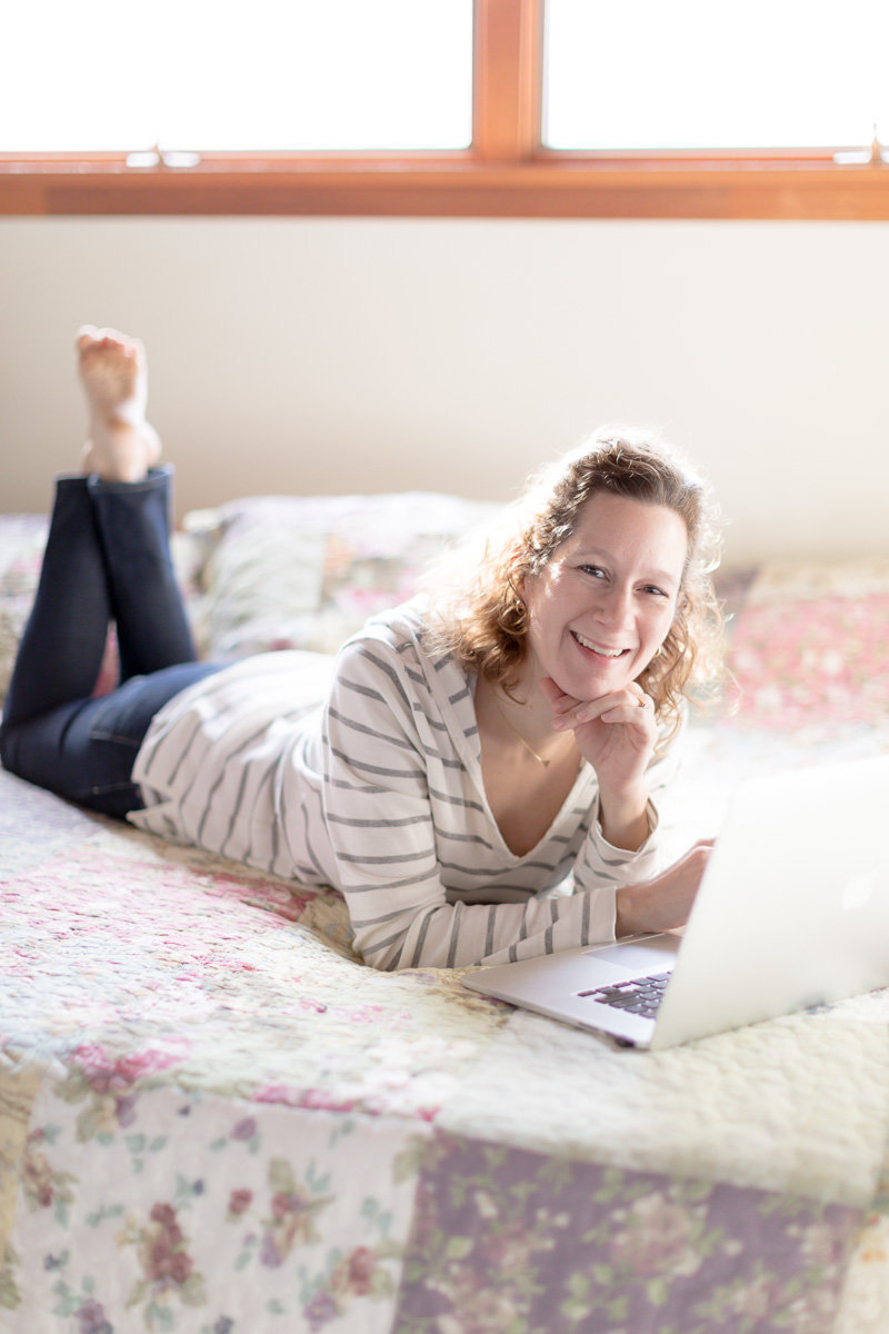 business owner lays on bed with laptop and smiles for branding picture