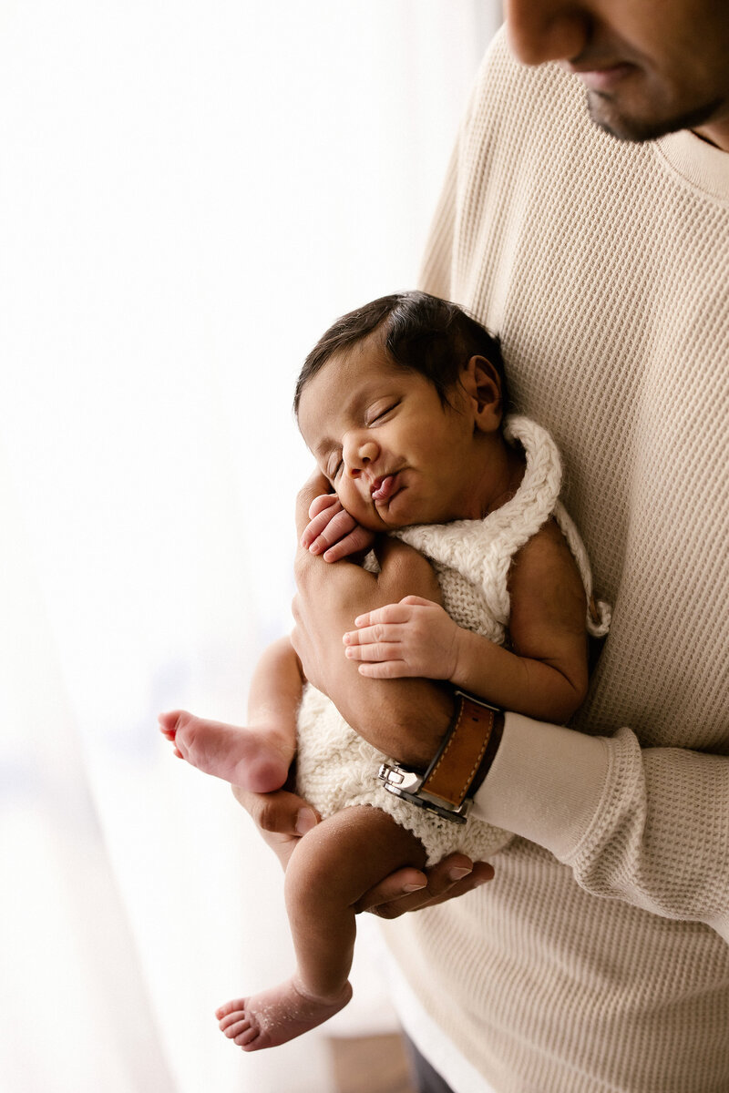 A newborn baby is held by his father during a newborn studio photoshoot with aimee kelly photography