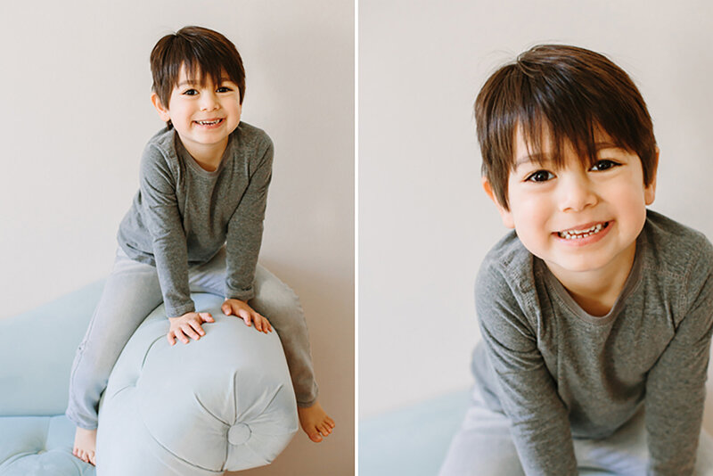 A child straddling the arm of a blue couch and smiling at the camera during a child portrait session in Daniele Rose Photography's studio