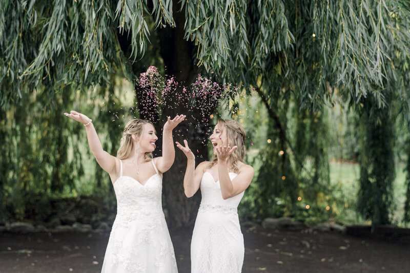 brides throw confetti in the air and smile at one another