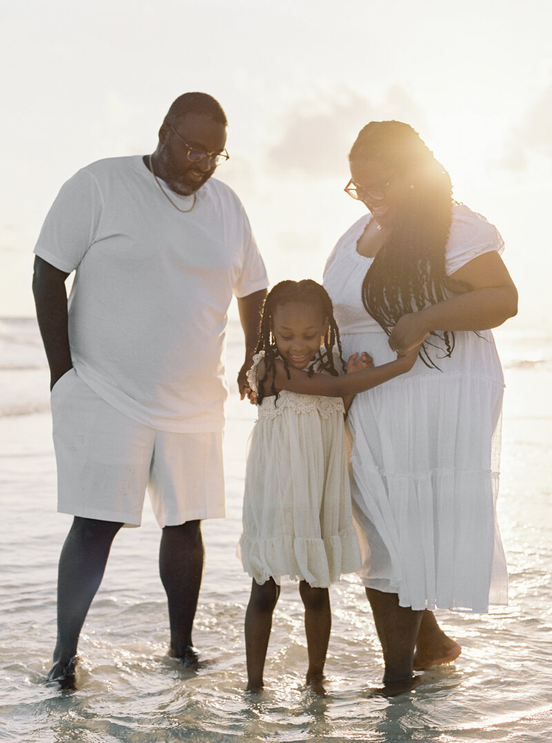 A girl with her mom and dad dressed in white for their family photos in Rosemary Beach, Florida.