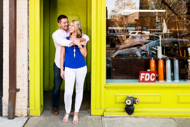 Couple poses for engagement photos in a green doorway in downtown Raleigh