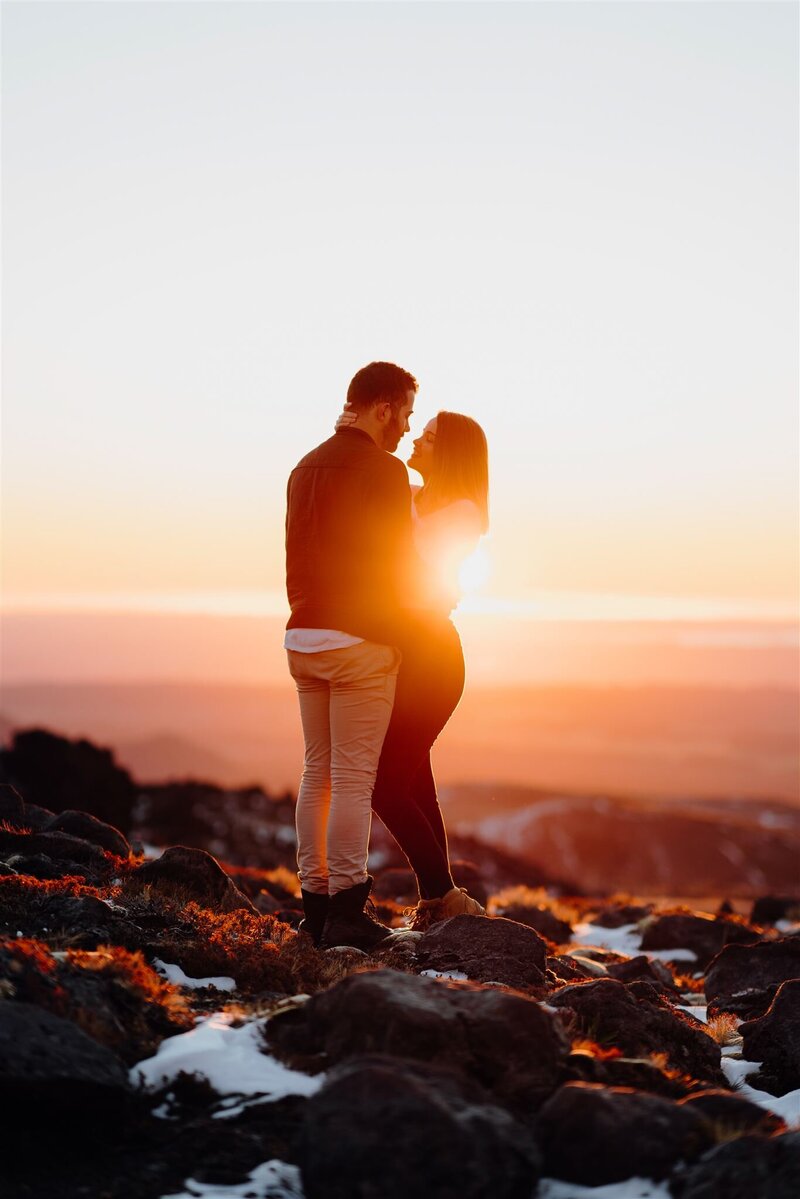 A couple standing on the rocks and snow at the top of Mt Ruapehu during an engagement photoshoot with Waikato Photographer Haley Adele Photography