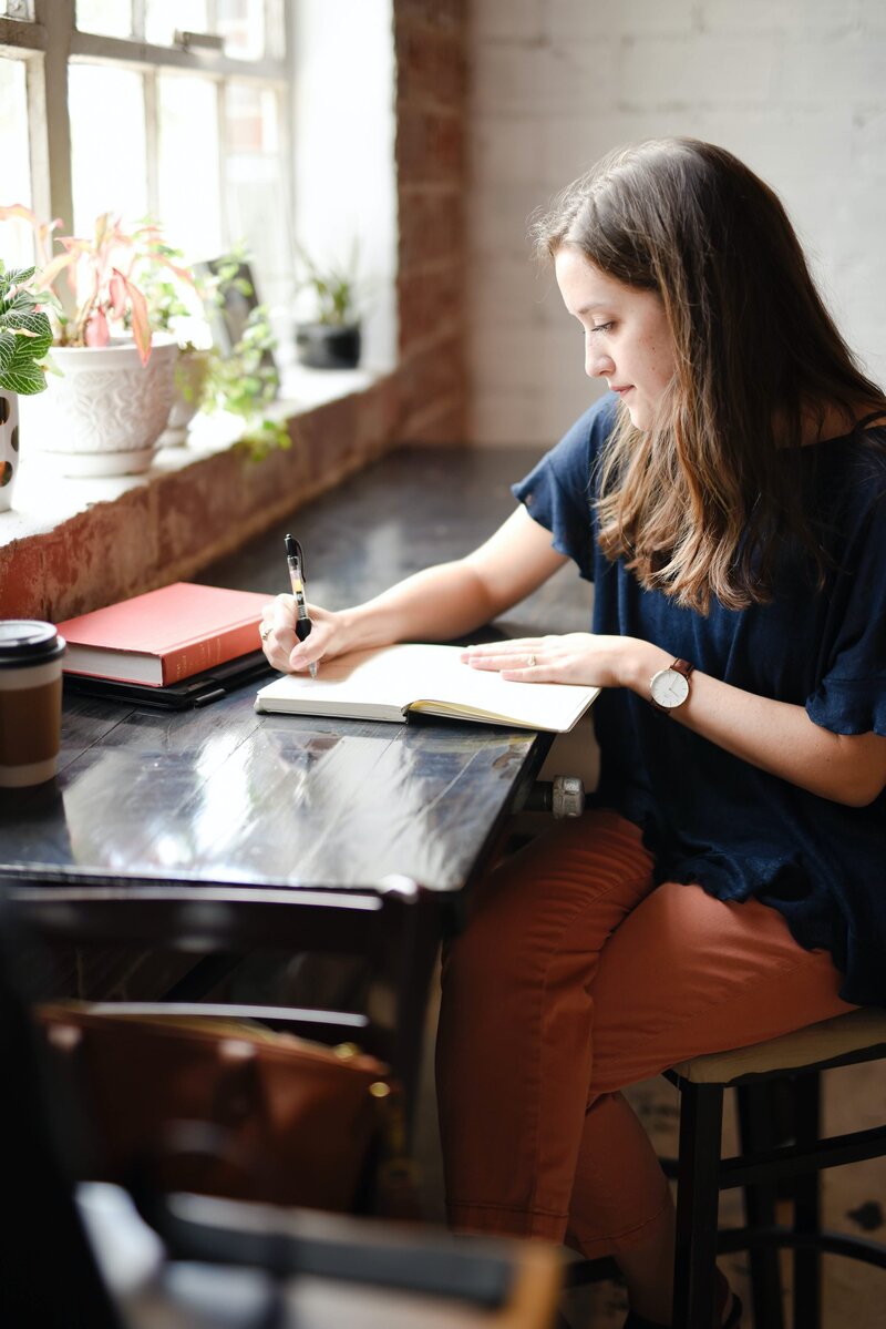 Woman writing in a notebook at a window-side counter top