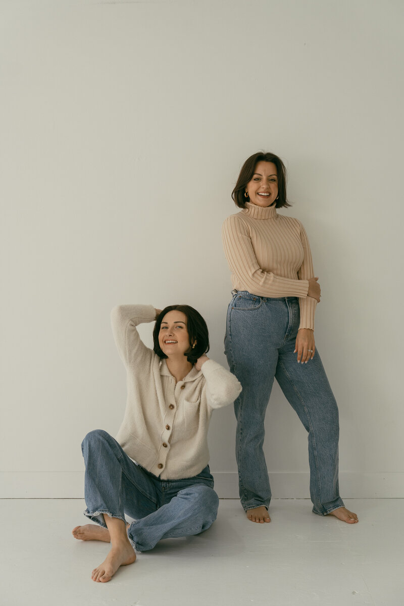 Two women smiling, one seated the other standing to pose.