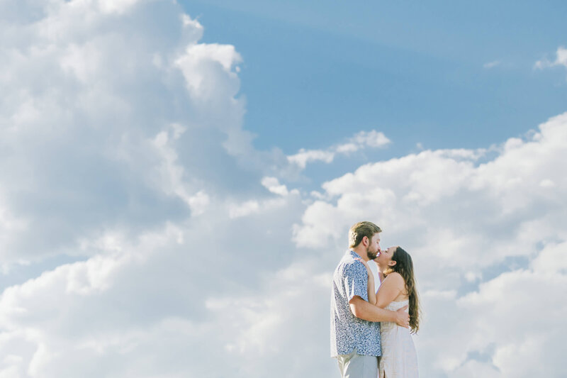 Couple kissing on dock seeing blur skies and clouds