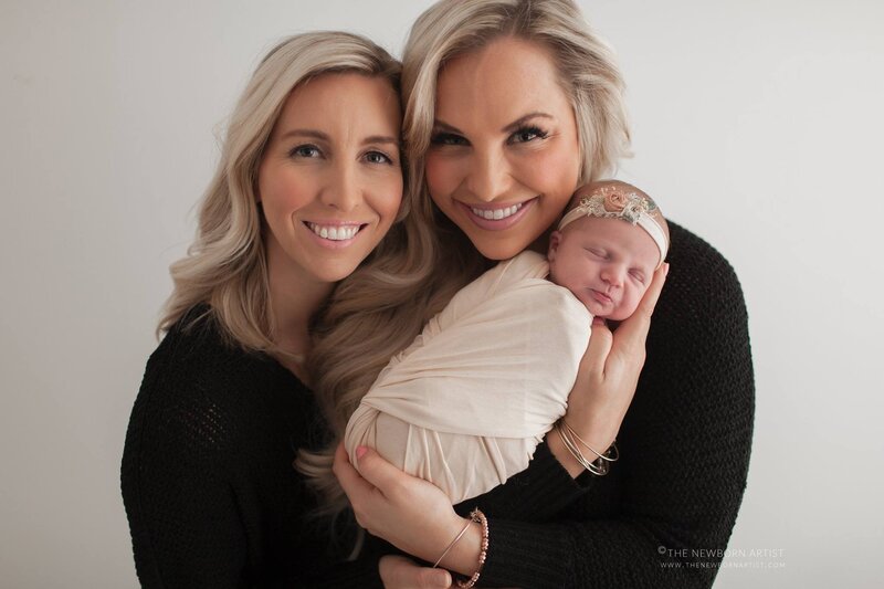two mothers holding adopted newborn baby girl smiling with white background
