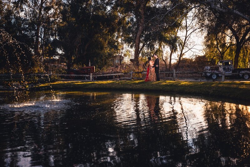 Bride and Groom in Indian wedding attire embracing by the lake at Lake Oak Meadows wedding venue in Temecula.