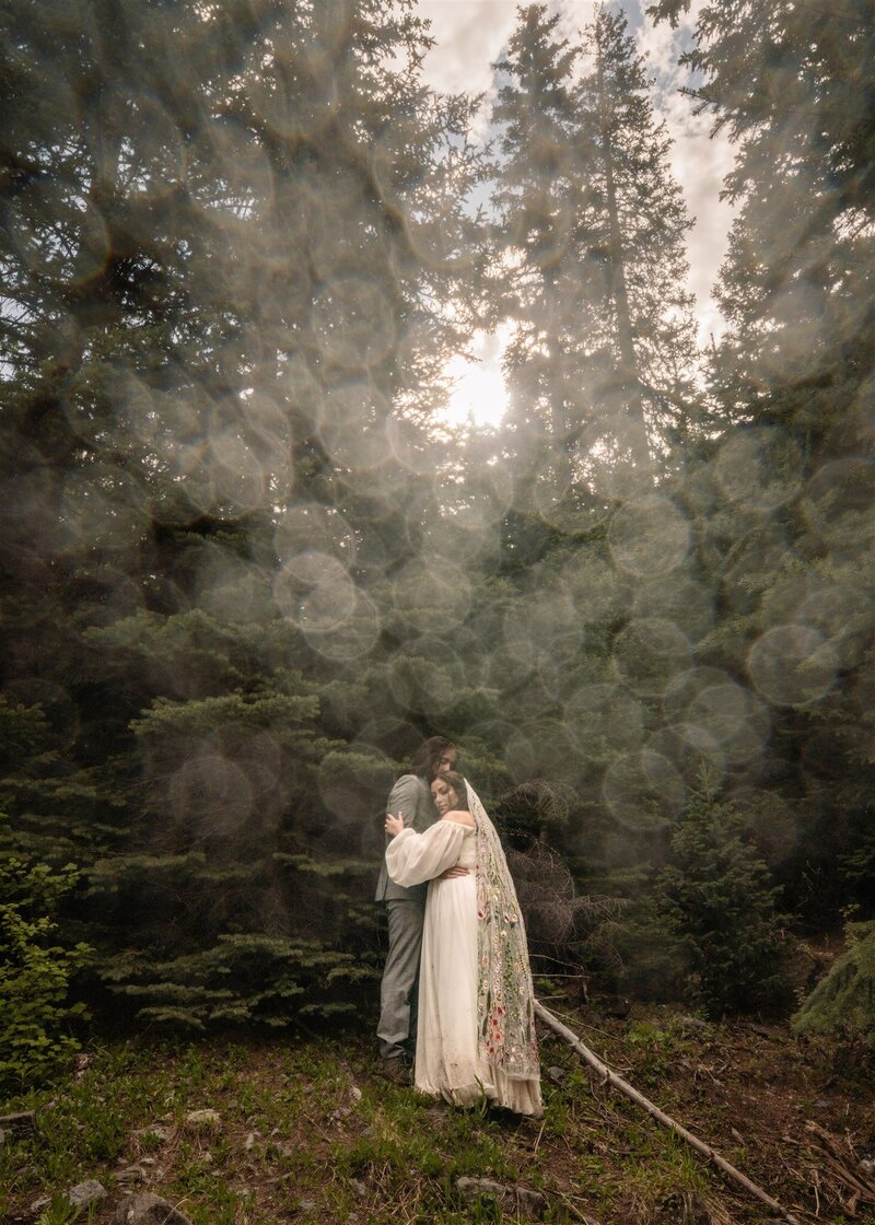 after learning how to elope in Washington State, a bride and groom embrace in a lush, green forest. water texturizes the camera lens to create a softening effect