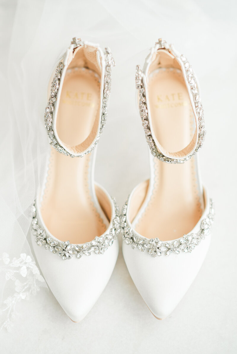 A detail shot of a bride's white and bejeweled wedding shoes.