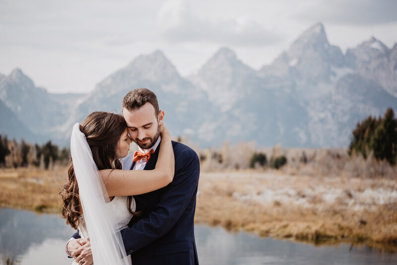 review for jackson hole photographers from a bride who had a grand teton wedding with her husband embracing her as she wraps her arms around his neck romantically