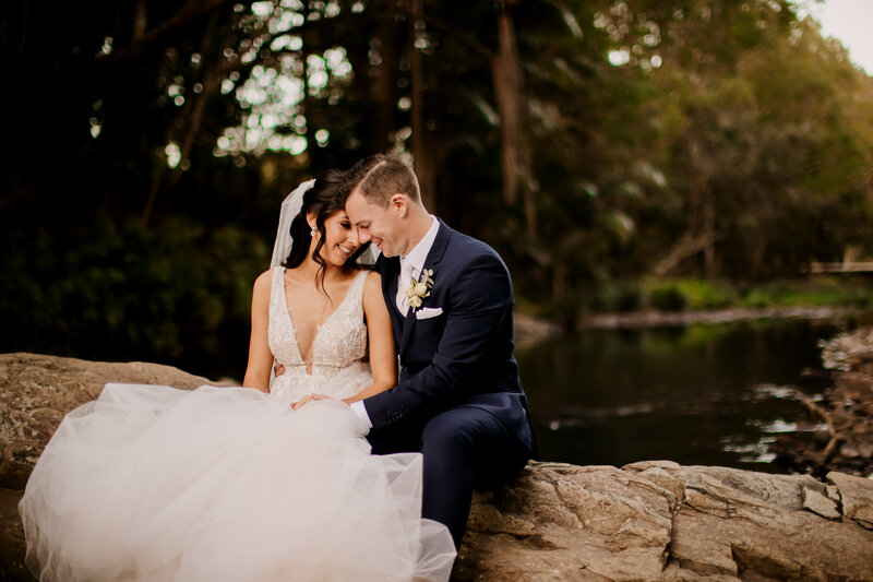 Bride and Groom sitting on a rock as they lovingly leans in close to each other.