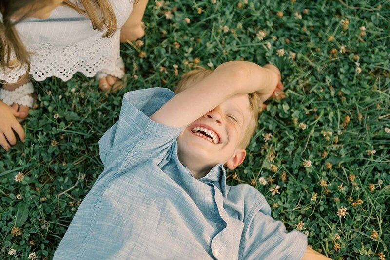 Little boy in blue shirt lying down on the grass and laughing
