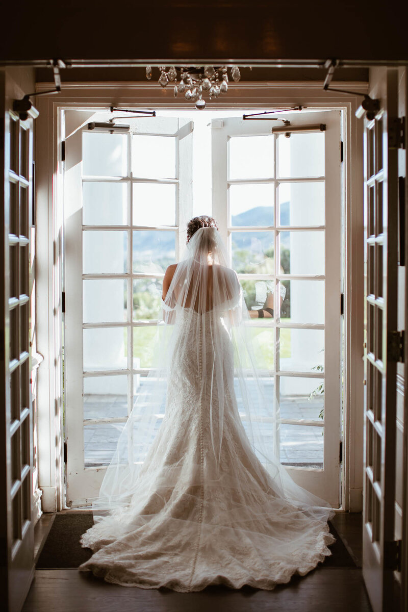bride peers out window at manor house