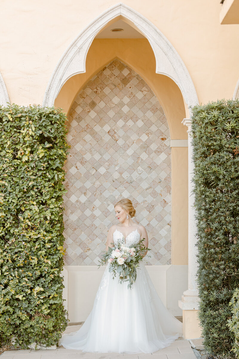 Beautiful bride poses under archway with her bouquet on wedding day