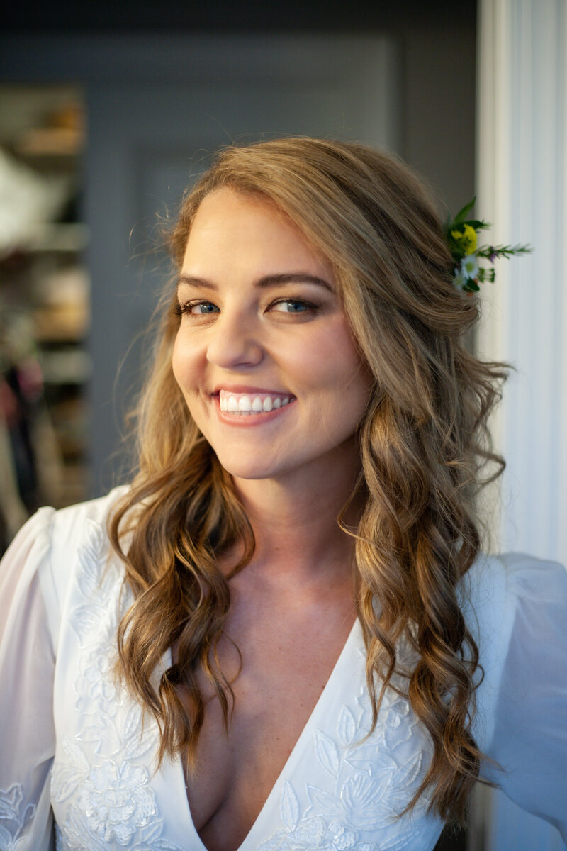 A bride with flowers in her curly blonde hair smiling with natural makeup vienna virginia