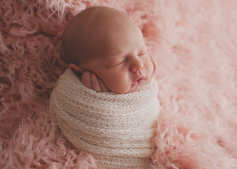 baby girl wrapped in pretty wrap in pink fur with hands on face sleeping