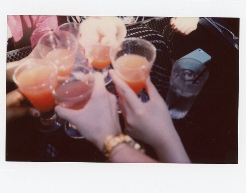 Polaroid of five friend's hands cheer-sing red drinks together