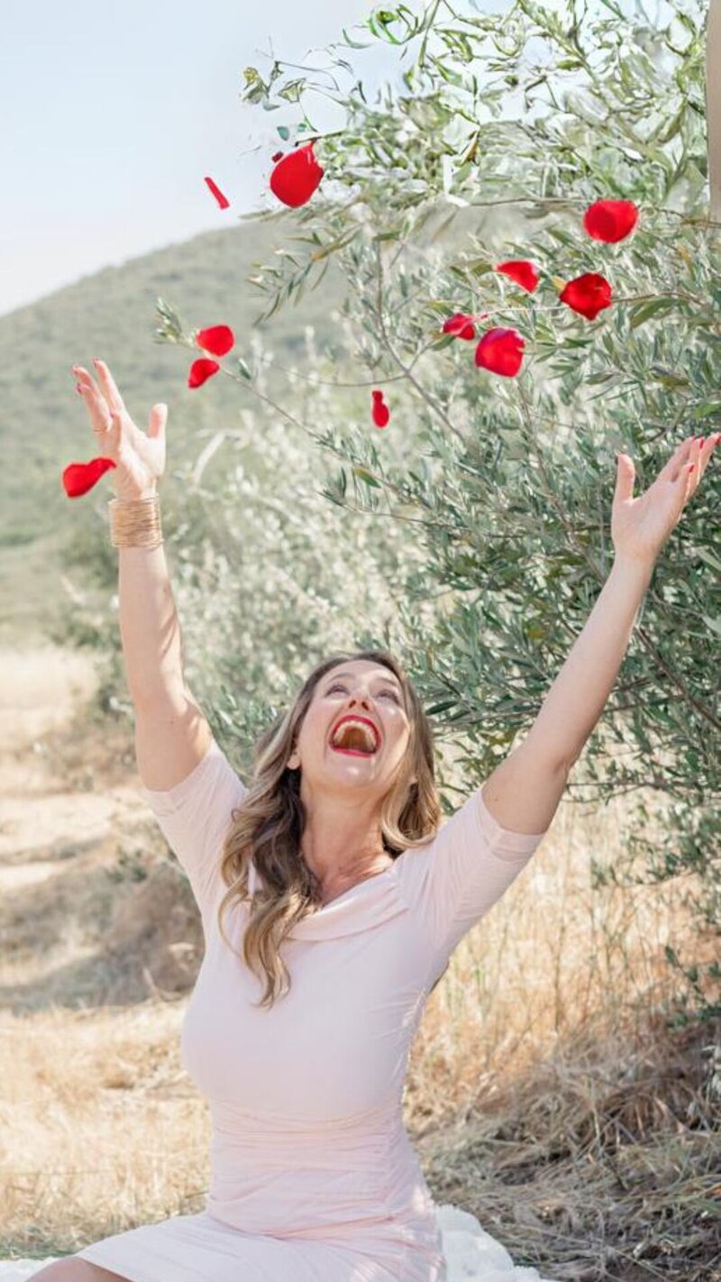 Keri Nola throwing roses petals in the air on a blanket in a grassy field