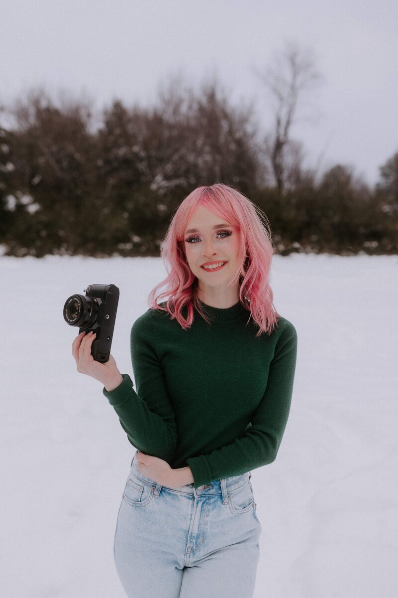 A girl with pink hair is looking off to the side smiling. She is wearing an emerald green floral lace dress and black hat.  She is an elopement photographer based out of Arkansas.