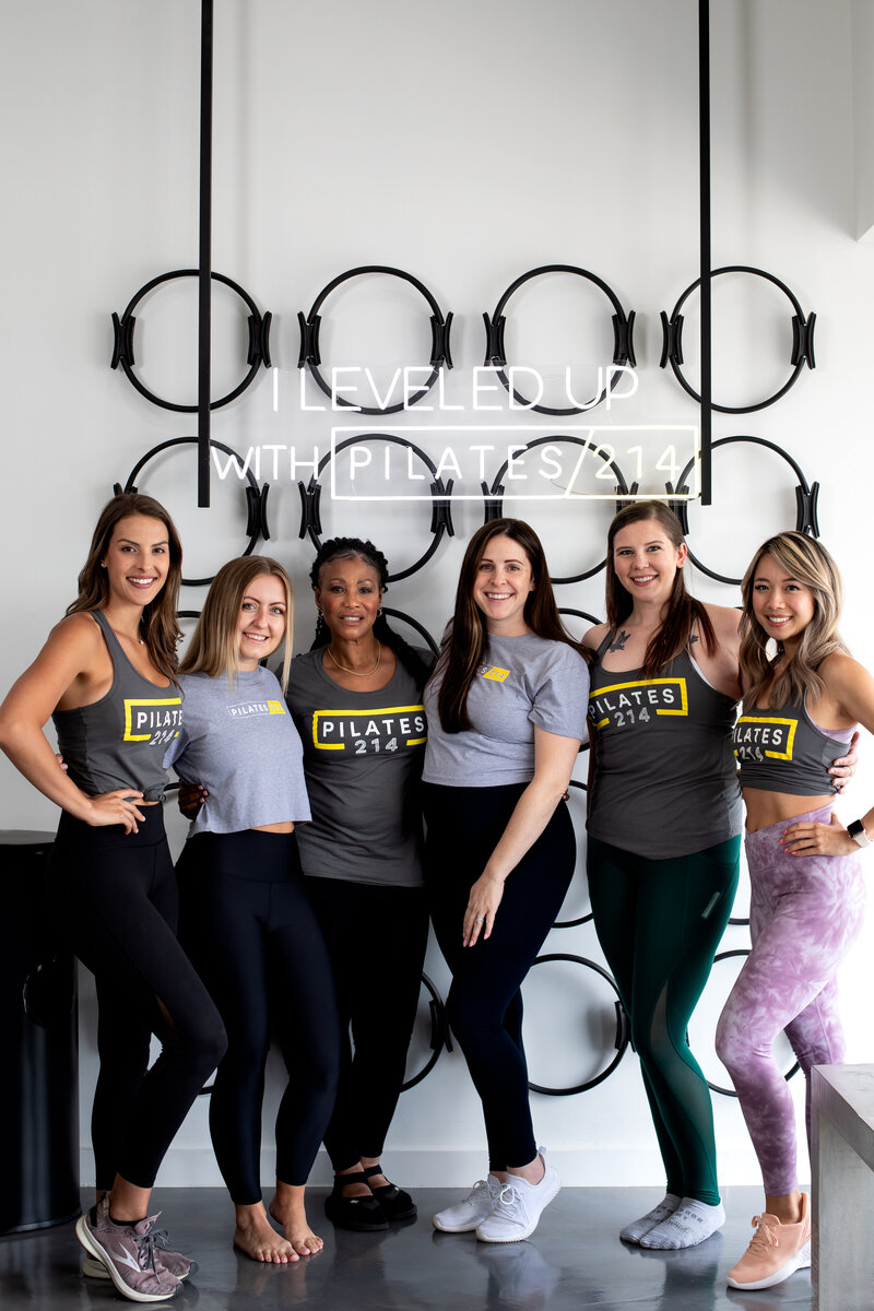 Group of Pilates214 Pilates instructors standing in front of neon I Leveled Up with Pilates214 sign in Dallas studio.